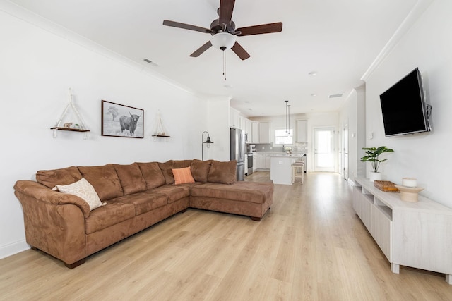 living area with visible vents, a ceiling fan, light wood-style flooring, and crown molding