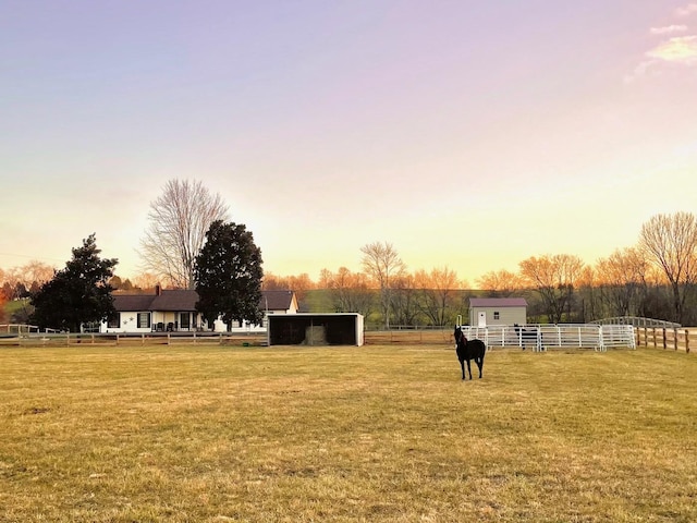 yard at dusk featuring an outbuilding and fence