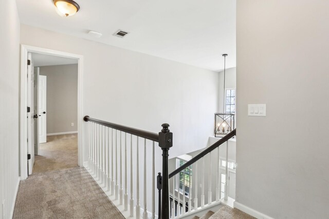 hallway featuring baseboards, carpet flooring, visible vents, and an upstairs landing