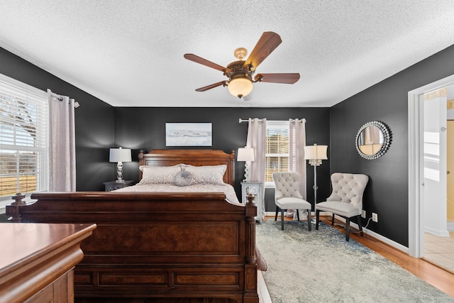 bedroom featuring a textured ceiling, baseboards, a ceiling fan, and light wood-style floors