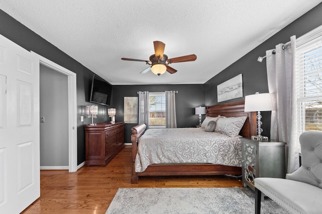 bedroom featuring ceiling fan, a textured ceiling, baseboards, and wood finished floors