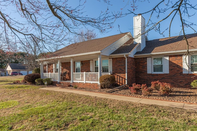 view of front of home with a porch, brick siding, roof with shingles, a front lawn, and a chimney