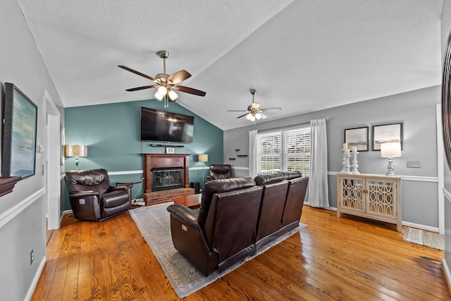 living area featuring a ceiling fan, lofted ceiling, hardwood / wood-style flooring, a textured ceiling, and a fireplace