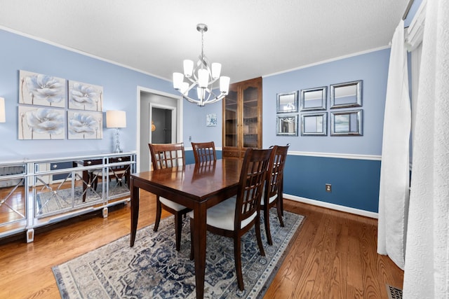 dining space featuring visible vents, crown molding, an inviting chandelier, and wood finished floors