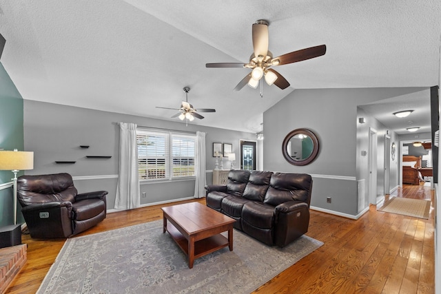 living room with lofted ceiling, wood-type flooring, baseboards, and a textured ceiling