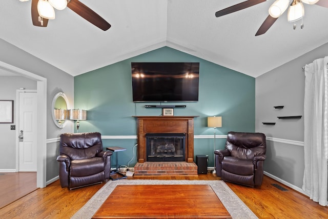 living area with visible vents, ceiling fan, wood finished floors, vaulted ceiling, and a fireplace