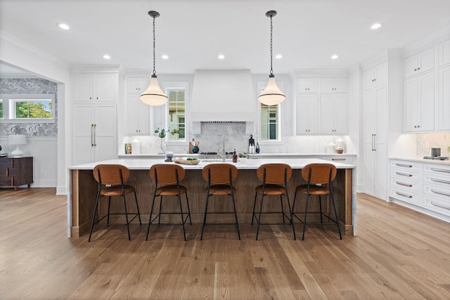 kitchen with white cabinets, light countertops, a large island with sink, and custom exhaust hood