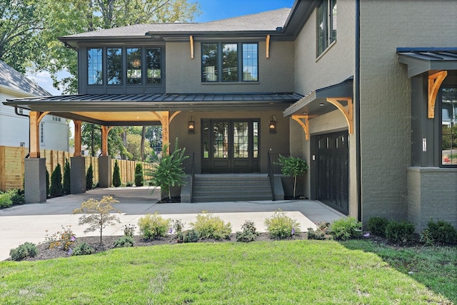 view of front of property featuring covered porch, brick siding, driveway, a front lawn, and a standing seam roof