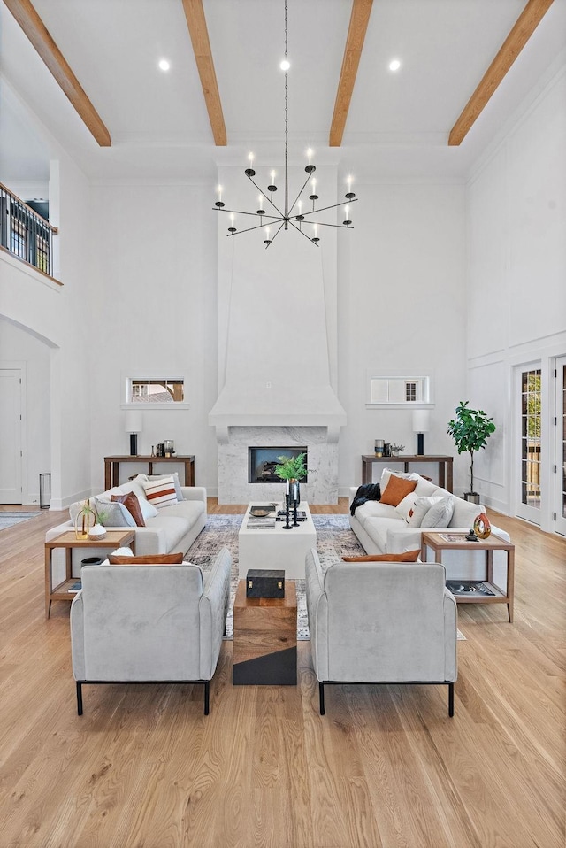 living room featuring a chandelier, light wood-type flooring, beam ceiling, and a premium fireplace