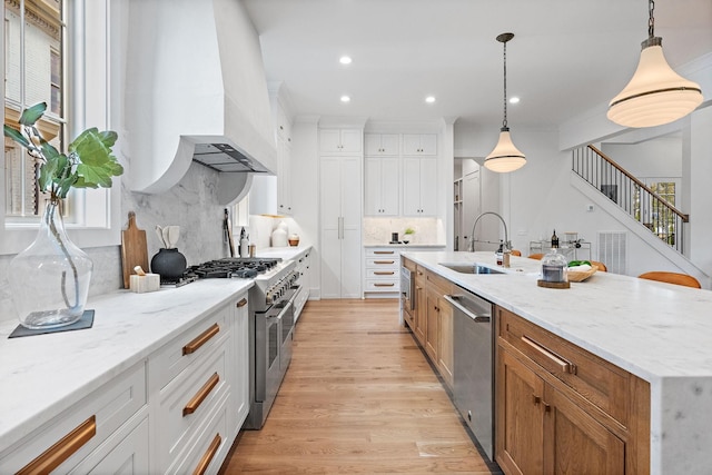 kitchen featuring stainless steel appliances, tasteful backsplash, white cabinets, a sink, and light wood-type flooring