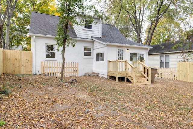 rear view of house with a shingled roof and fence