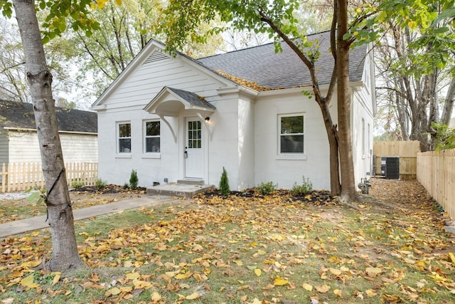 view of front facade with cooling unit, roof with shingles, and fence