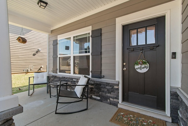 view of exterior entry featuring stone siding and covered porch