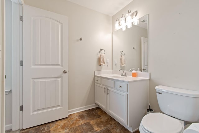 bathroom featuring stone finish flooring, toilet, vanity, and baseboards