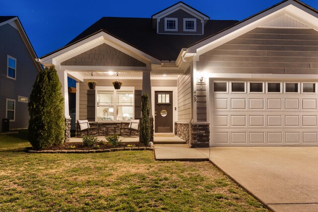 craftsman house featuring a lawn, stone siding, a porch, central AC, and a garage