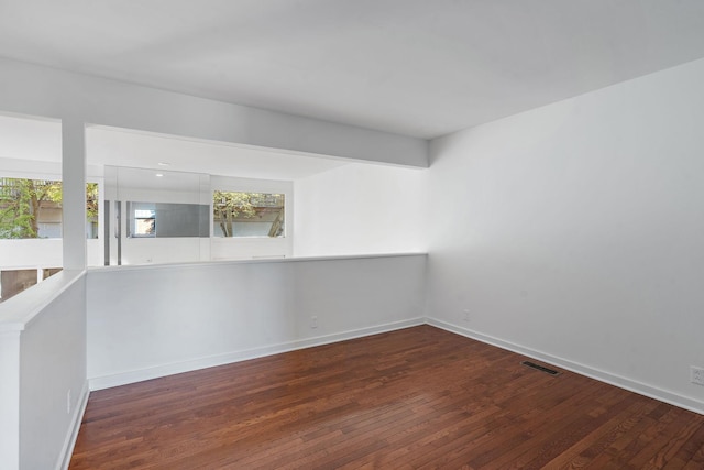 empty room featuring wood-type flooring, visible vents, and baseboards