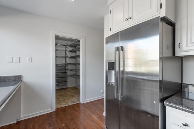 kitchen featuring dark stone counters, baseboards, white cabinets, dark wood-style floors, and stainless steel fridge