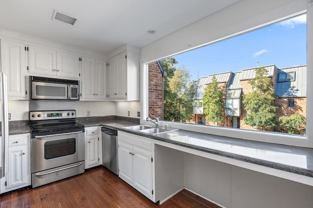 kitchen with dark countertops, appliances with stainless steel finishes, dark wood-style flooring, white cabinetry, and a sink