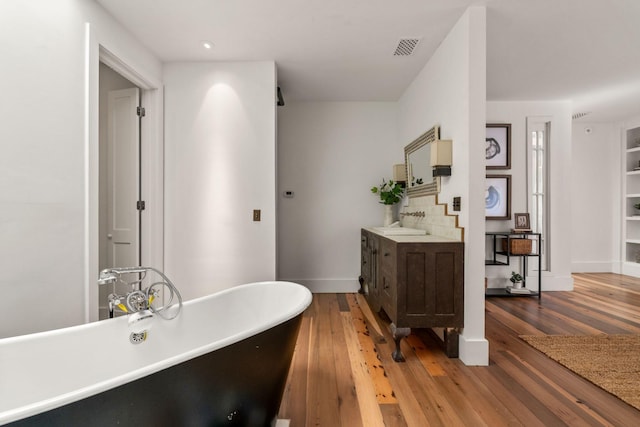 full bathroom with visible vents, a freestanding bath, vanity, wood finished floors, and baseboards