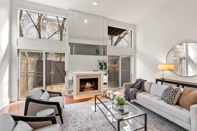 living room featuring a lit fireplace, wood finished floors, a towering ceiling, and recessed lighting