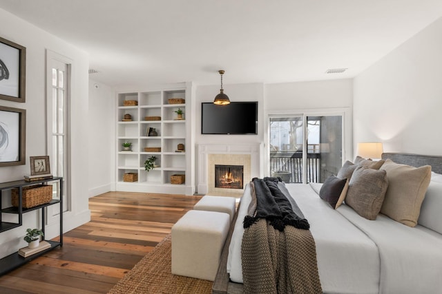 bedroom featuring access to exterior, visible vents, a tiled fireplace, and hardwood / wood-style flooring