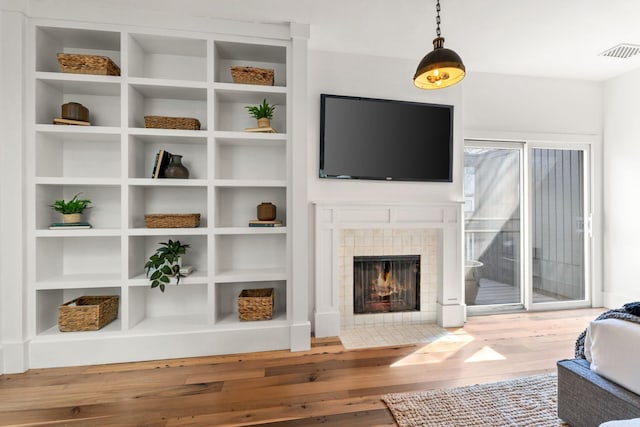 interior space featuring hardwood / wood-style flooring, visible vents, built in features, and a tile fireplace