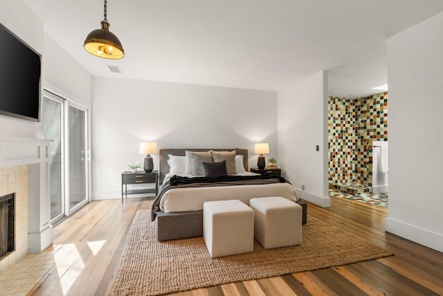 bedroom with light wood-type flooring, a fireplace, visible vents, and baseboards