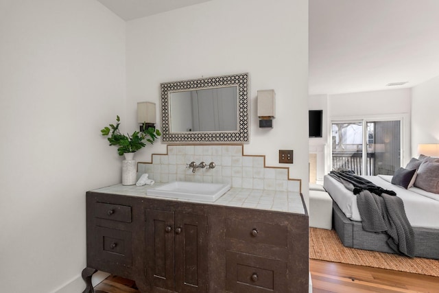 bathroom featuring wood finished floors, a sink, visible vents, and decorative backsplash