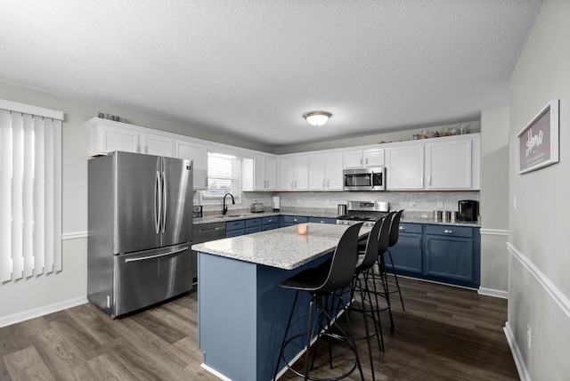 kitchen featuring dark wood-style floors, a breakfast bar area, appliances with stainless steel finishes, white cabinetry, and a sink