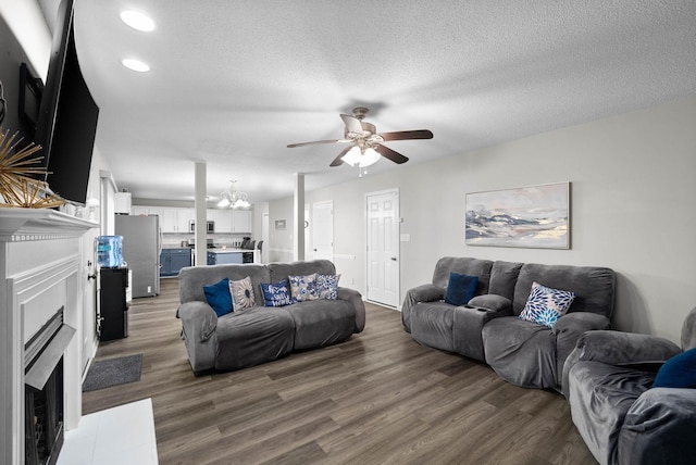 living area with recessed lighting, a fireplace with flush hearth, a textured ceiling, wood finished floors, and ceiling fan with notable chandelier