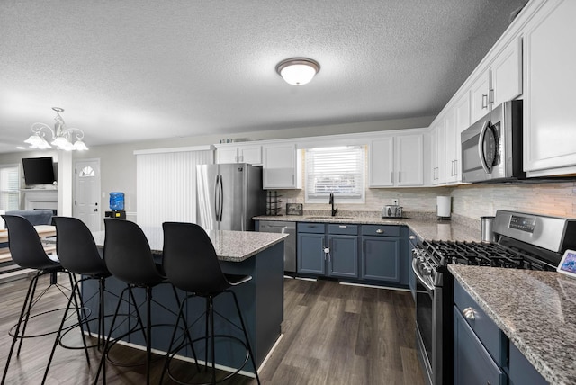 kitchen featuring a kitchen breakfast bar, dark wood-style flooring, stainless steel appliances, blue cabinetry, and a sink