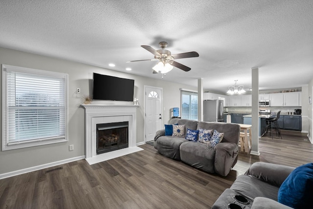 living area with baseboards, visible vents, dark wood-style floors, a fireplace, and ceiling fan with notable chandelier