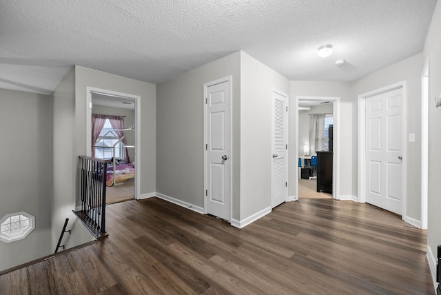 hall featuring dark wood-style floors, a textured ceiling, an upstairs landing, and baseboards