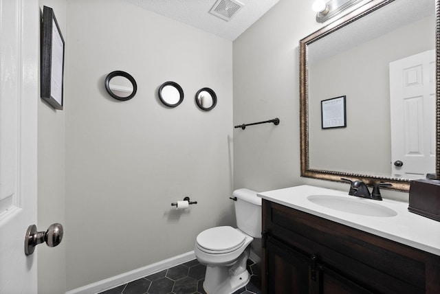 bathroom featuring toilet, vanity, baseboards, visible vents, and tile patterned floors