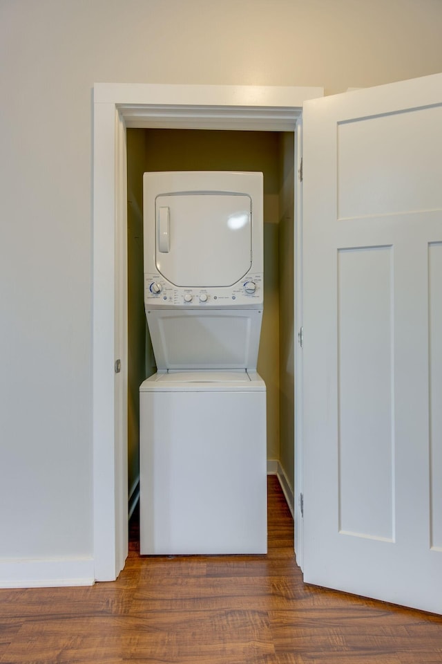 laundry area with laundry area, baseboards, stacked washing maching and dryer, and wood finished floors