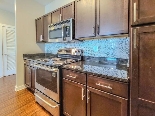 kitchen with dark brown cabinetry, appliances with stainless steel finishes, backsplash, light wood finished floors, and dark stone countertops