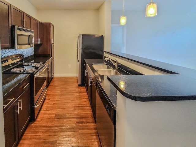 kitchen with dark countertops, appliances with stainless steel finishes, a sink, dark brown cabinets, and wood finished floors