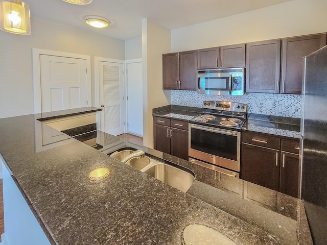 kitchen with a sink, dark brown cabinets, appliances with stainless steel finishes, tasteful backsplash, and dark stone countertops