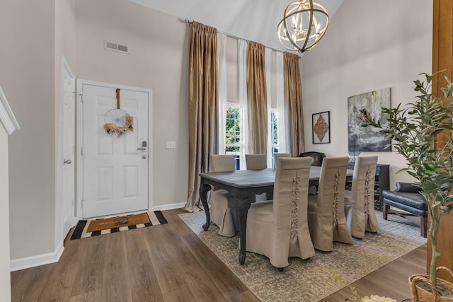 dining space featuring visible vents, a towering ceiling, an inviting chandelier, wood finished floors, and baseboards