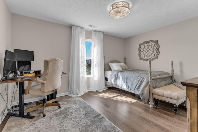 bedroom with a textured ceiling, wood finished floors, visible vents, and baseboards