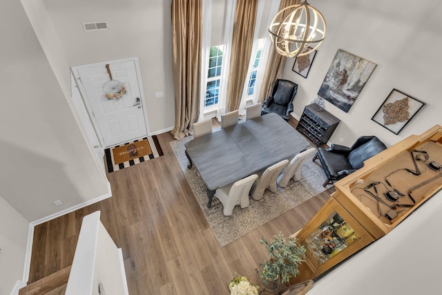 interior space featuring baseboards, visible vents, a towering ceiling, wood finished floors, and a notable chandelier