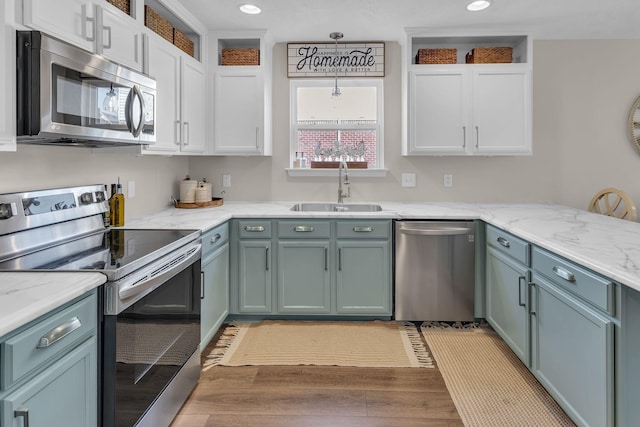 kitchen with appliances with stainless steel finishes, light stone countertops, white cabinetry, a sink, and recessed lighting