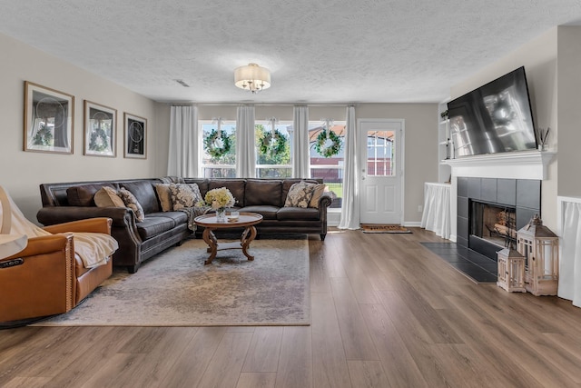 living room with a tile fireplace, plenty of natural light, a textured ceiling, and wood finished floors