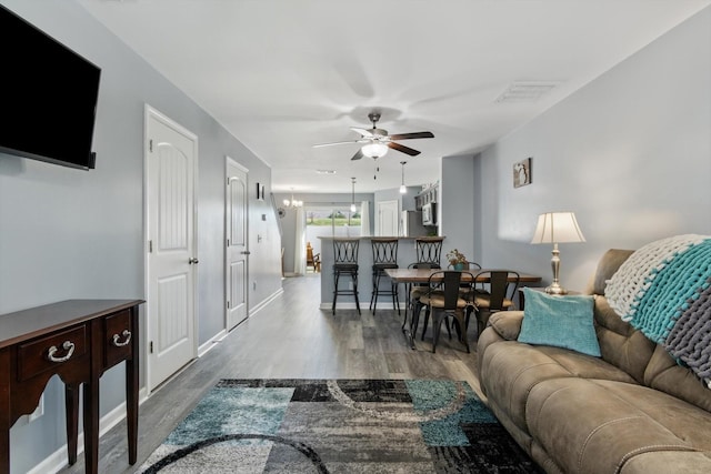 living room featuring ceiling fan with notable chandelier, wood finished floors, visible vents, and baseboards