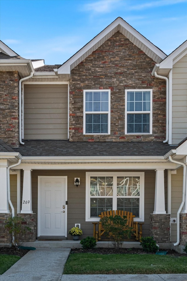 townhome / multi-family property with stone siding, a porch, and a shingled roof