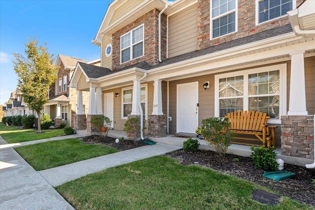 view of front of property with covered porch, a shingled roof, stone siding, and a front yard