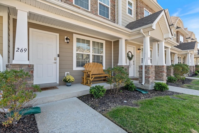 doorway to property with a shingled roof and a porch