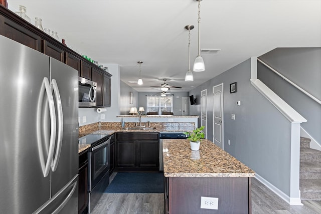 kitchen featuring a peninsula, stainless steel appliances, a sink, and wood finished floors