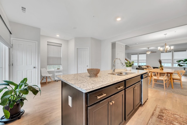 kitchen with light stone counters, a sink, a kitchen island with sink, light wood-style floors, and stainless steel dishwasher