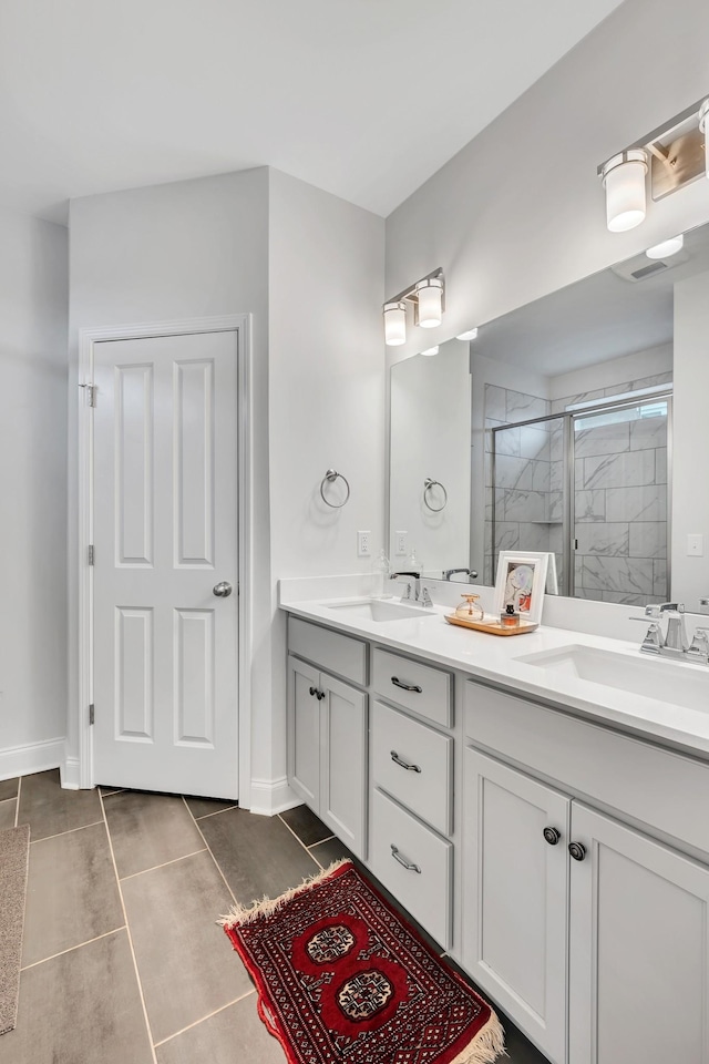 bathroom featuring double vanity, a stall shower, a sink, and baseboards